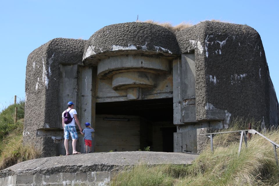 Een man en een jongetje houden elkaars hand vast bij een enorme bunker.