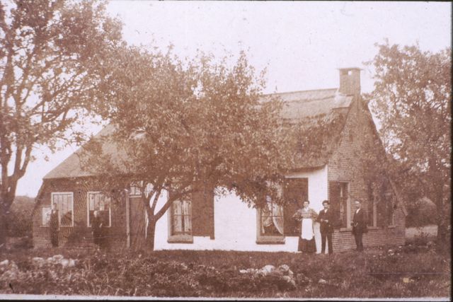 Een oude foto van mensen die voor hun huis in de koloniën staan.