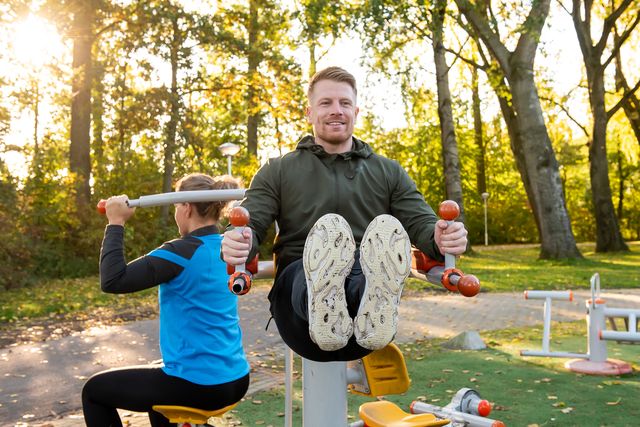 Een man en vrouw zijn samen aan het sporten in het bos. Ze doen verschillende oefenen bij de outdoor fitness in het van Tuyllpark.
