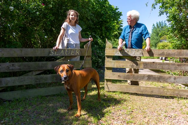 Wiepkje Hoekstra met hond en gids bij open hek in de zon.