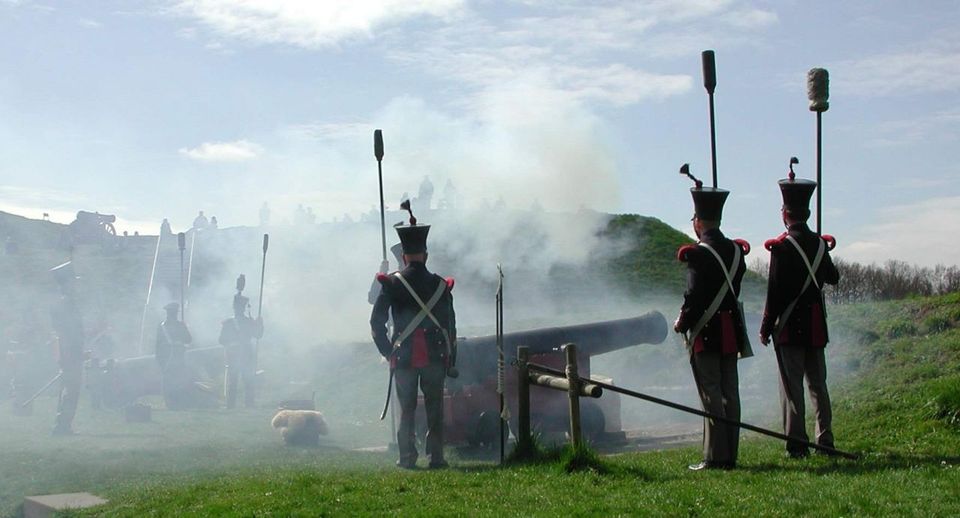 Een groep mannen in ouderwetse uniformen schiet met oude kanonnen.