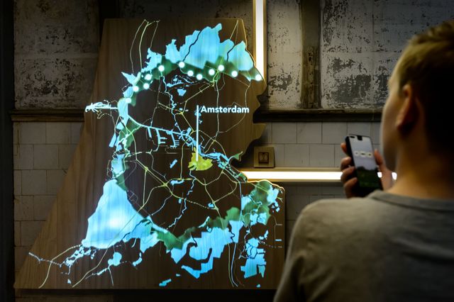 Een bezoeker bekijkt een weergave van de Stelling van Amsterdam en luistert naar een verhaal.