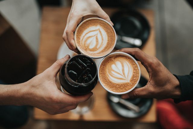 Een luchtfoto van twee kopjes koffie en een glas drinken met ijs. De kopjes koffie hebben een leuk figuur in het kopje.
