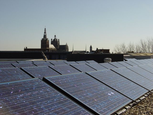 Foto van zonnepanelen op het dak van het Stadskantoor, met op de achtergrond de Sint-Jan.