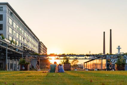 Een foto van Eindhoven Strijp-S gemaakt door VisitBrabant waarbij 2 personen zitten naar een zonsondergang kijken in een industrieelgebied
