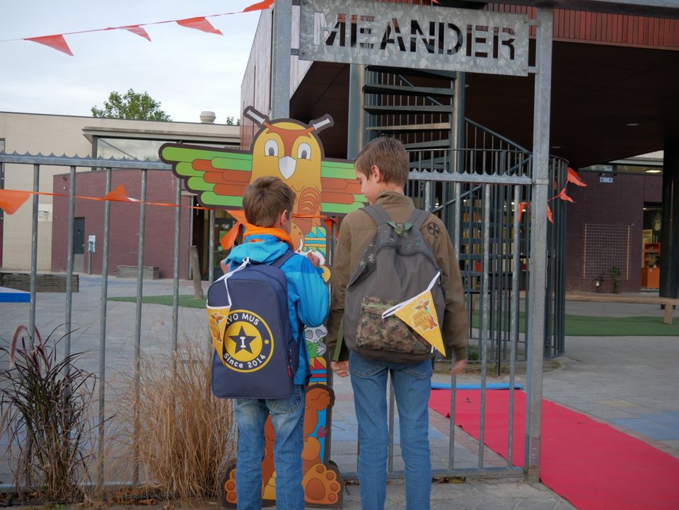 Foto van twee jongetjes die bij de ingang van KC Meander staan met twee rugzakjes.