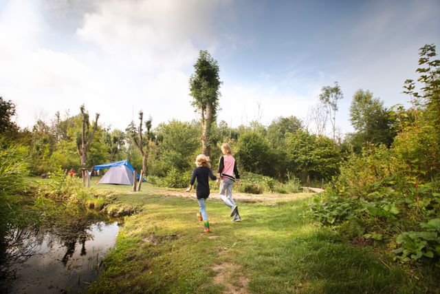 Meisjes rennen door de natuur richting een tent, wild kamperen in Lelystad, Flevoland