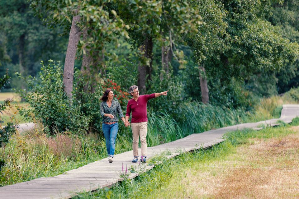 Een man en vrouw wandelen over een houten vlonderpad door het Drentsche Aa gebied in Drenthe