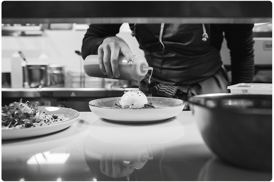 Een zwart wit foto van een kok in TWAALF Restaurant en Bar die een gerecht afmaakt