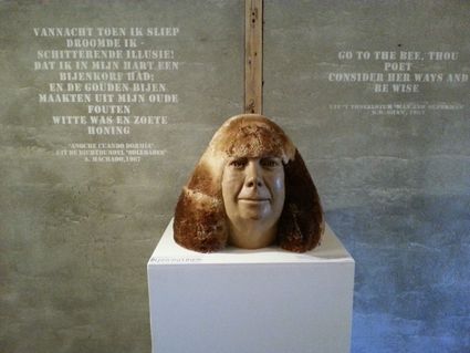 Een hoofd op een sokkel met daarop een bijenraad als haar met op de achtergrond tekst over het bijenmuseum van Kunstfort bij Vijfhuizen.