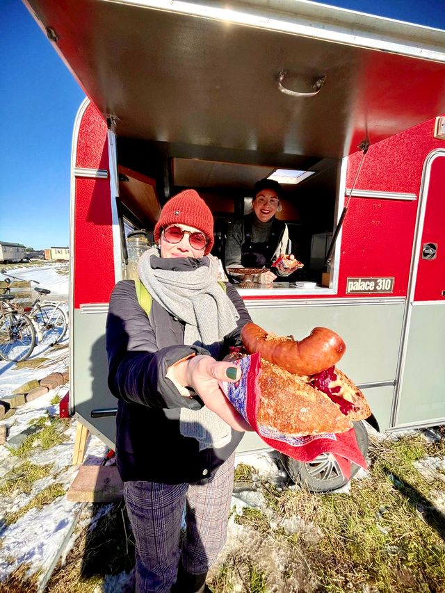 De boerderijbox foodtruck op de achtergrond, op de voorgrond een vrouw met een broodje worst
