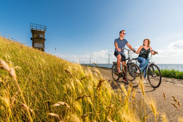 Vooraanzicht van een man en vrouw die op de dijk bij Rotterdamse Hoek in de Noordoostpolder fietsen.
