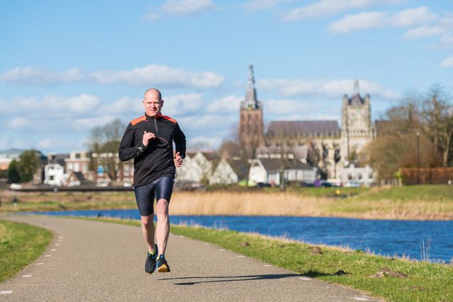 Foto van een man die aan het hardlopen is in Het Bossche Broek. Op de achtergrond is de Sint-Janskathedraal te zien.