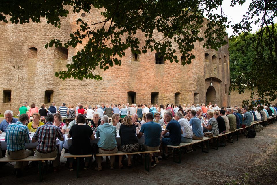 Mensen eten aan lange tafels voor het torenfort van Honswijk
