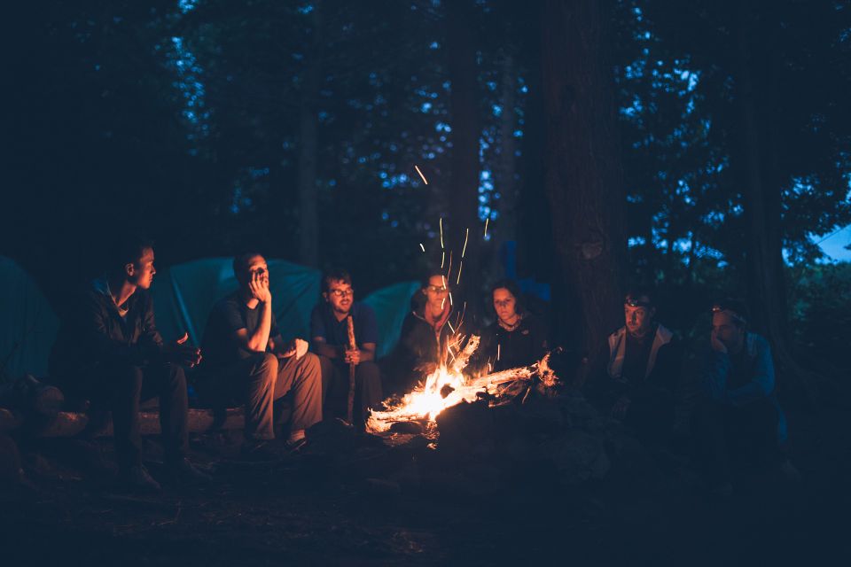 Een groep mensen zit in het donker rondom het kampvuur.