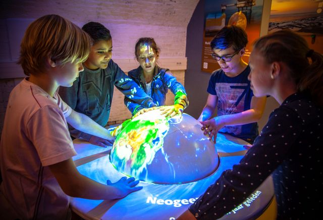 Een groep van vijf kinderen speelt met een bol waarop een projectie van de wereld te zien is.