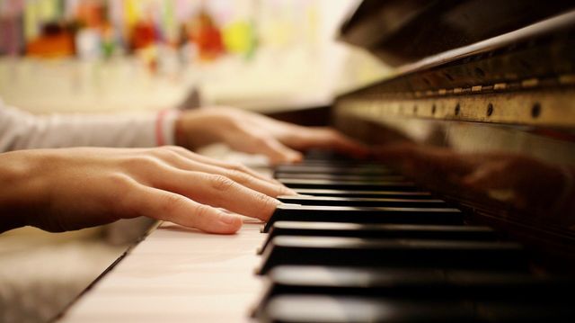 Iemand speelt piano en haar vingers op de piano worden van dichtbij gefotografeerd.