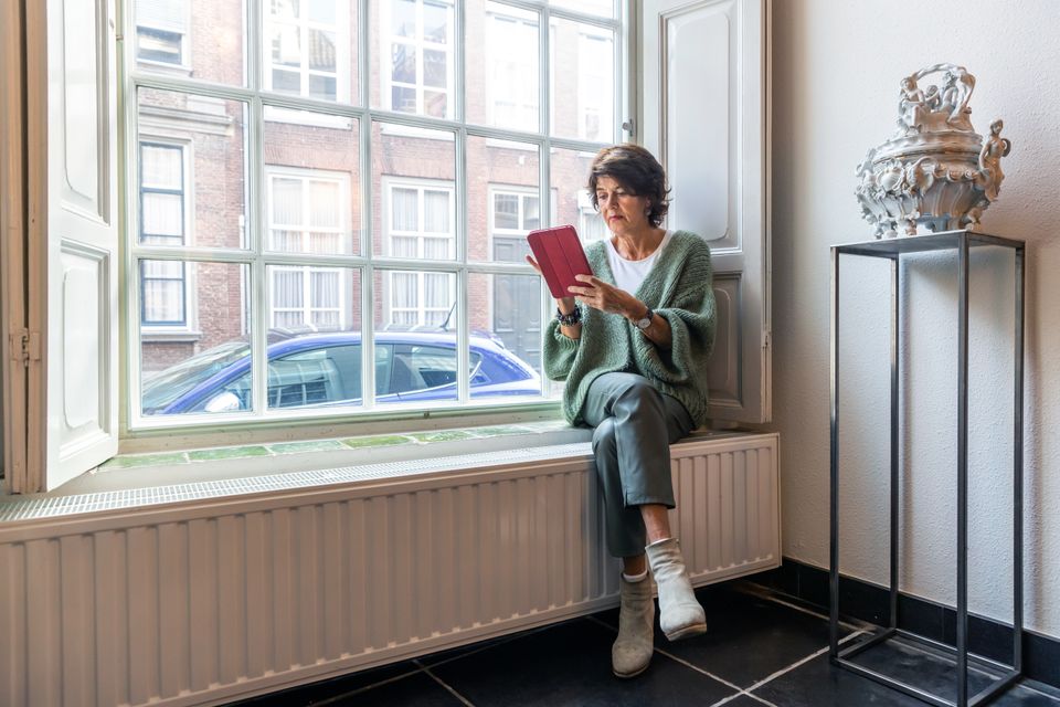 Foto van Willeke Hoek, zittend op de vensterbank met een tablet in haar handen.