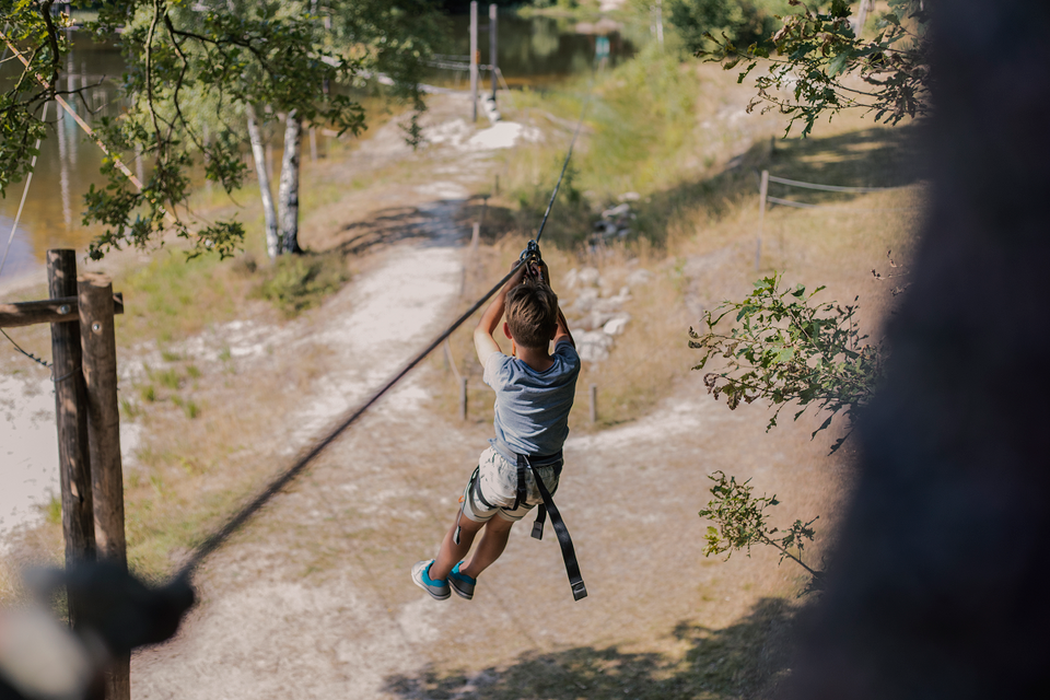 Ein Junge geht im Kletterpark mit der Seilbahn auf die andere Seite des Sees.