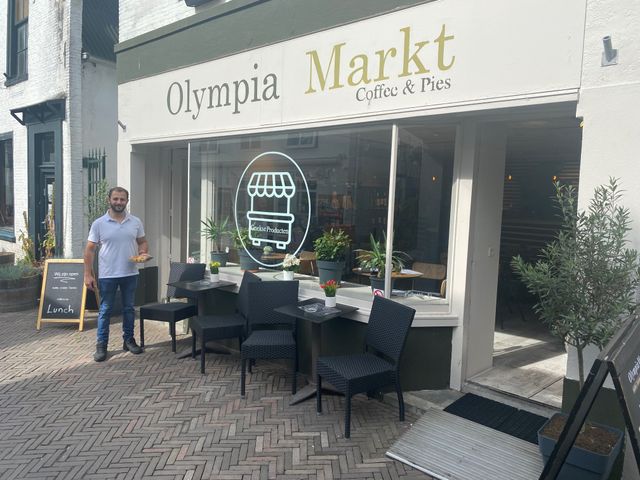 Een foto van het voor aanzicht van Olympia markt samen met de eigennaar.
