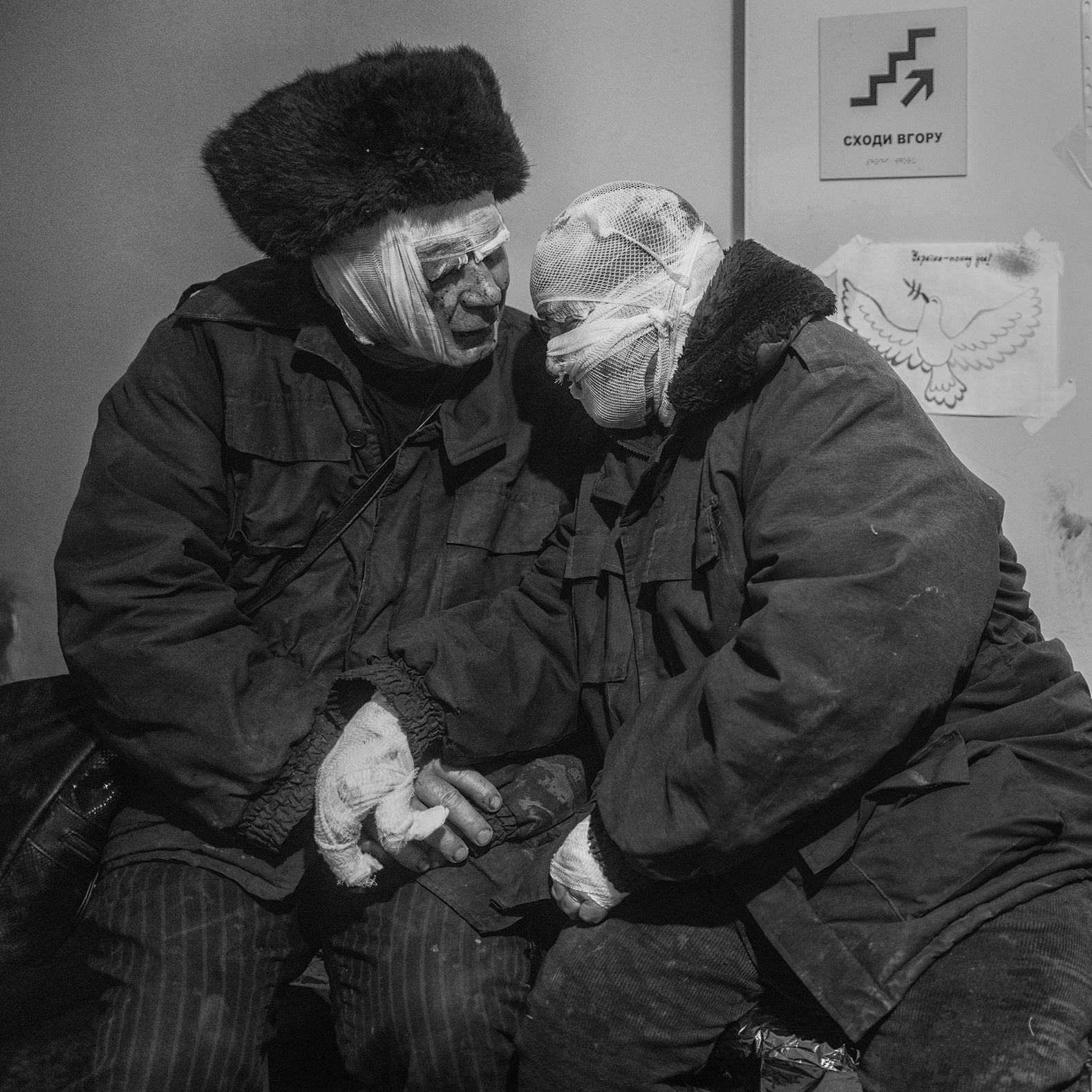 Een zwart wit foto van twee oude mensen die ingewinkeld zijn met verband en dikke jassen ook heeft een een muts op.
