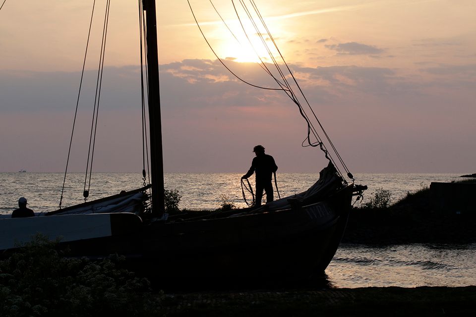 een zeilboot met een man op dek onder de zonsondergang.