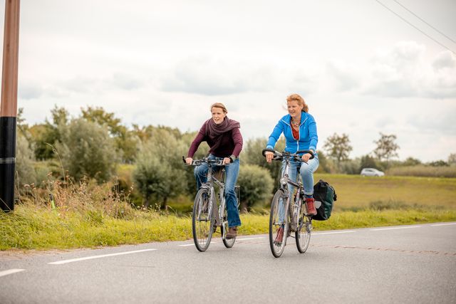 Twee vrouwen fietsen over een asfalt fietspad door een groene omgeving.