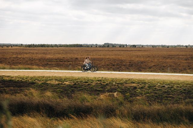 Een man en een vrouw fietsen door het uitgestrekte veenlandschap van het Bargerveen.