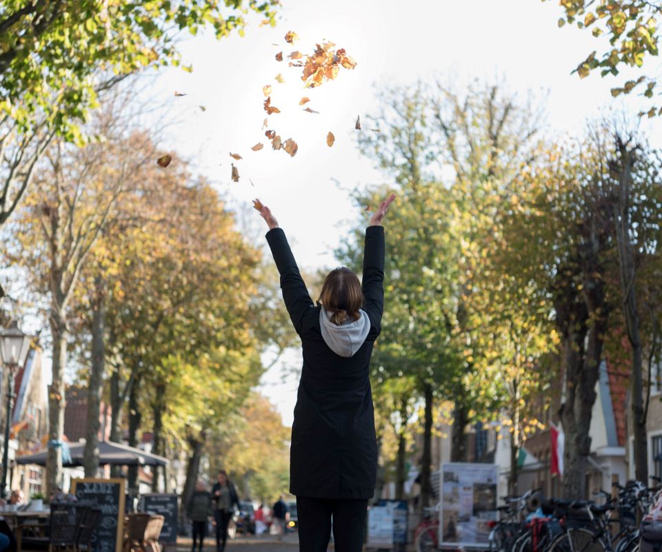 Vlieland vrouw gooit herfst bladeren op in dorpsstraat