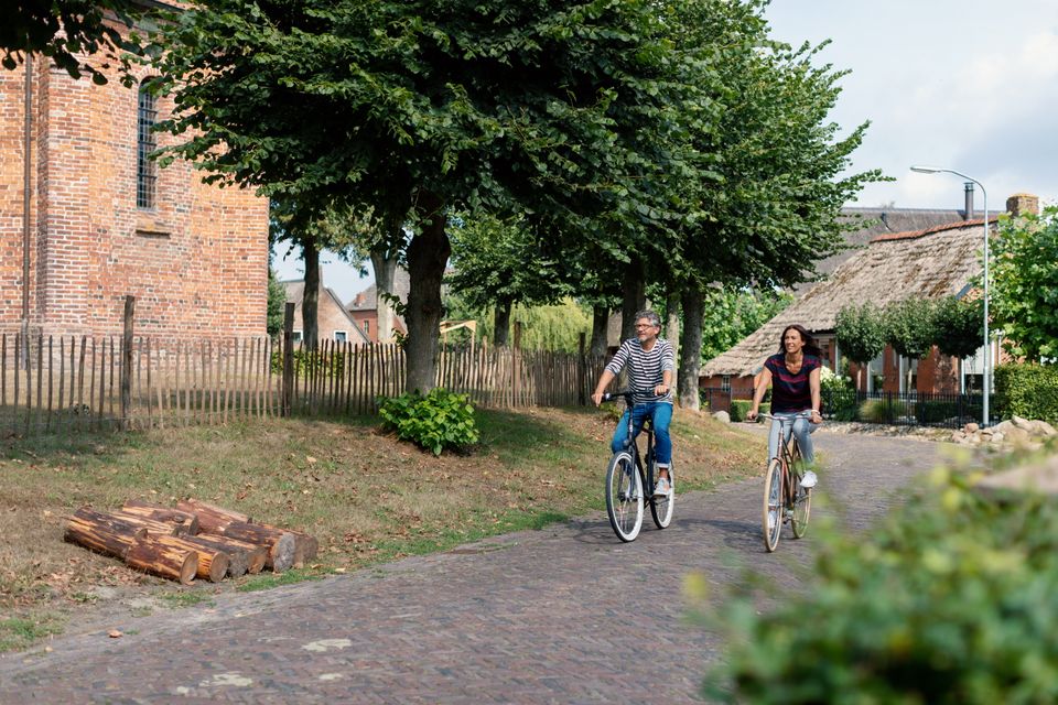 Een man en vrouw fietsen in de zomer door een dorp in Drenthe.