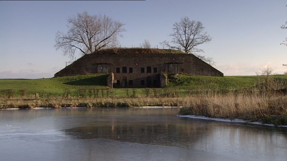 Een oud bakstenen fort gezien vanaf een water partij. Het fort is overgroeid met planten en bomen.