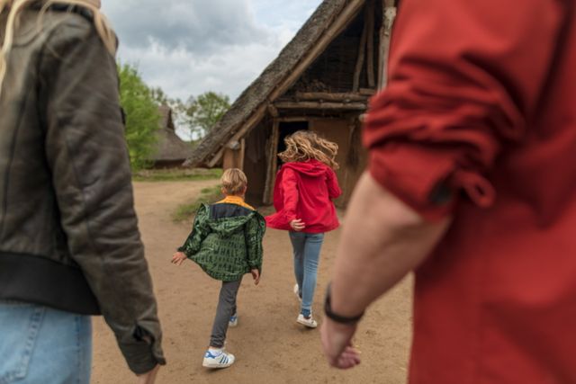 Kinderen rennen naar een oude boerderij in het hunebedcentrum, gevolgd door hun ouders.