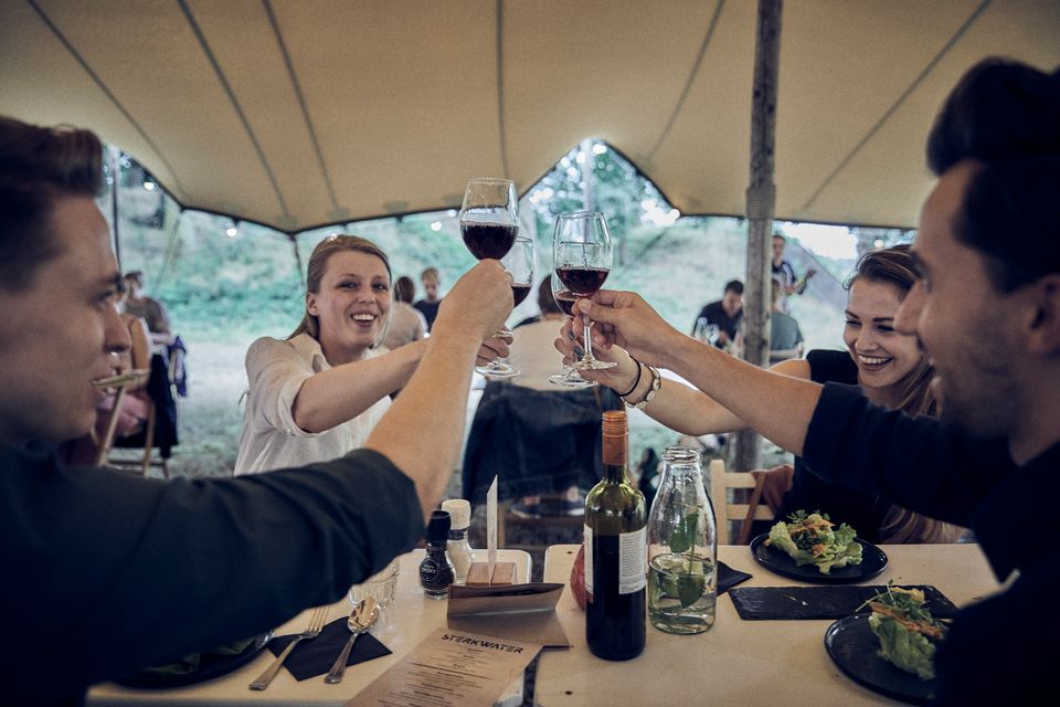 Een groep mensen proost met glazen rode wijn in een tent op het terrein van een fort.