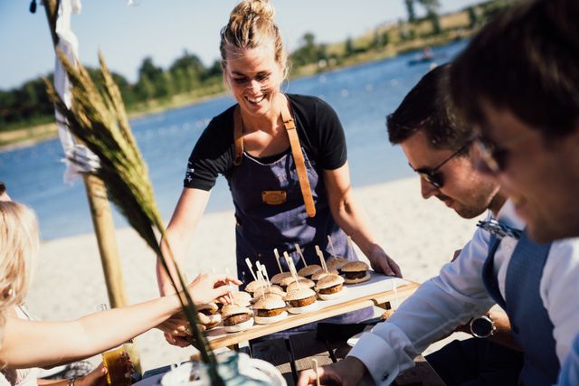 Een tafel op een terras aan het strand wordt bediend door een medewerker die ze hapjes serveert. Bij de Wellerwaard in Emmeloord in de Noordoostpolder.
