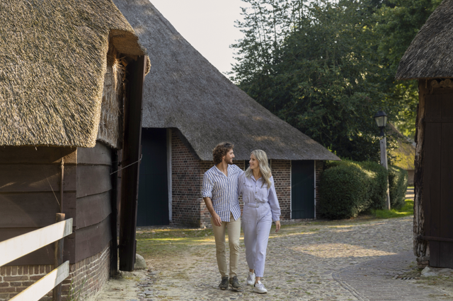 Een man en een vrouw wandelen in Orvelte over een oeroude klinkerweg tussen de authentieke saksische boerderijtjes.