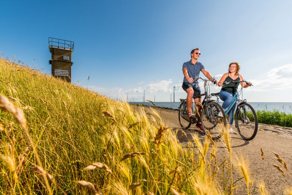 Vooraanzicht van een man en vrouw die op de dijk bij Rotterdamse Hoek in de Noordoostpolder fietsen.