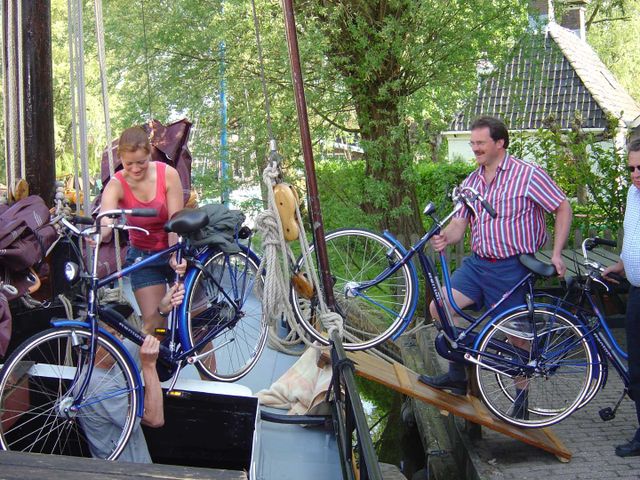 een vrouw en een man die hun fiets op een boot proberen te tillen in balk.